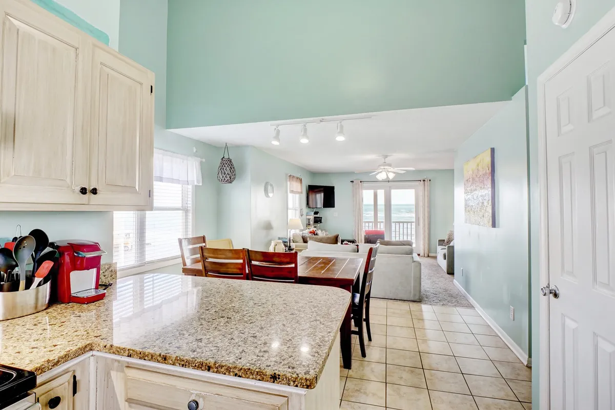 A wide, inviting open-concept space that seamlessly brings together the granite-topped kitchen, dining table, and living area with a comfortable couch. Large windows bathe the room in natural light and frame breathtaking ocean views, creating a social hub perfect for gatherings.