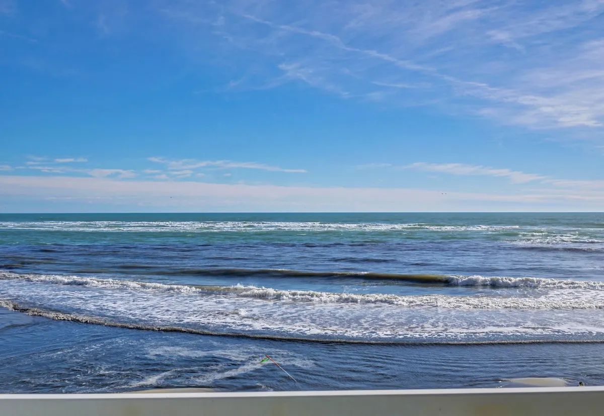 An unobstructed, wide-angle view of the ocean waves rolling in under a clear blue sky, with a distant horizon. The image focuses purely on the beauty and expanse of the ocean itself, inviting viewers to imagine peaceful sunrises and sunsets.