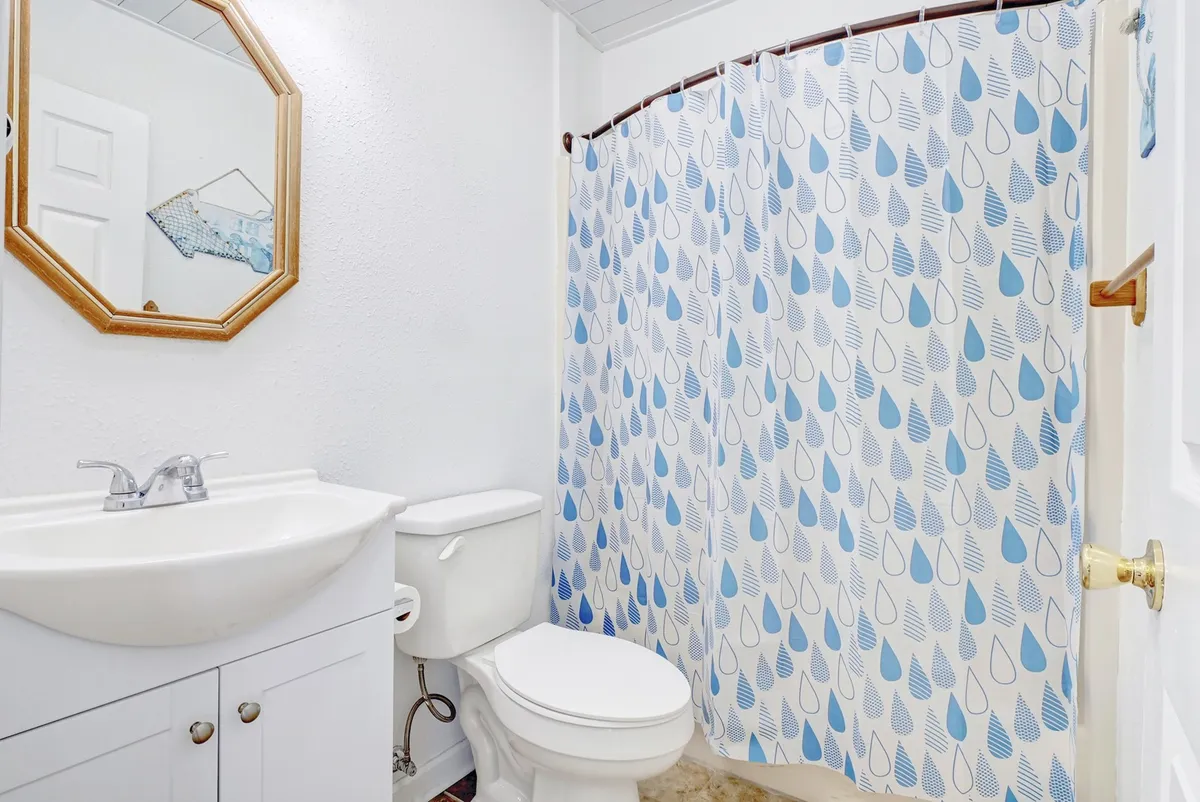 A bright, well-maintained bathroom with a vanity, sink, toilet, and shower curtain. The clean, inviting space suggests convenience for personal routines after a day at the shore.