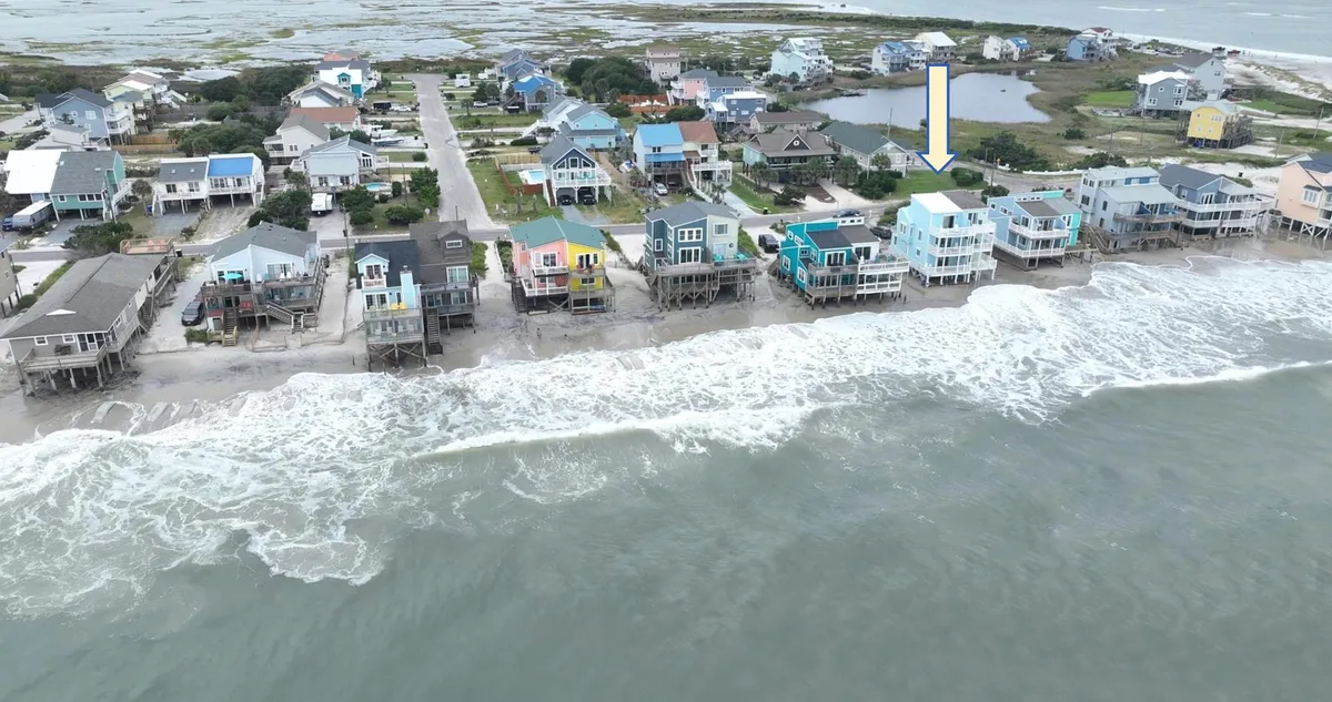 A tranquil view of beachfront houses facing the ocean, with gentle waves lapping onto the sandy shore under a peaceful sky. The image captures the inviting stretch of beach and the proximity of the homes to the water, suggesting easy access for morning walks or romantic evenings.