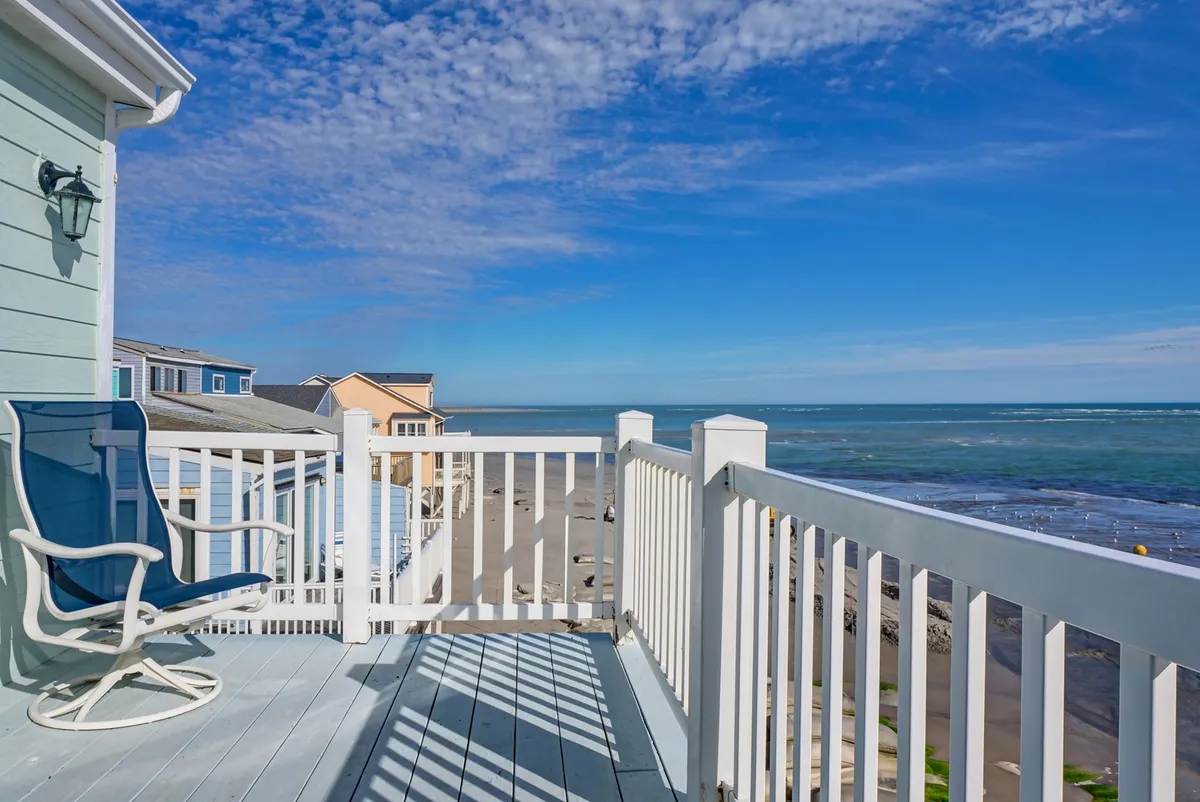 The image features the spacious balcony of a single-family beach house overlooking the serene North Topsail Beach shoreline. The inviting lounge chair and sleek balcony railing set the stage for unobstructed ocean views, with a sweeping blue sky above. The tranquil scene suggests ultimate relaxation, with the gentle sound of waves and the possibility of sunrise vistas.